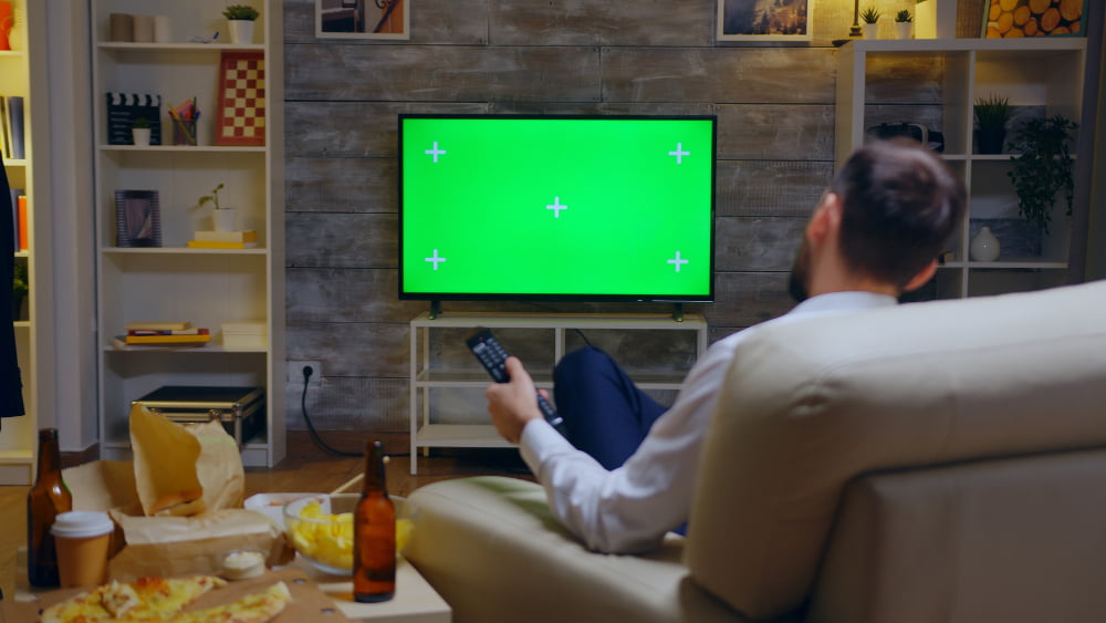 back view young man sitting couch front tv with green screen using remote control