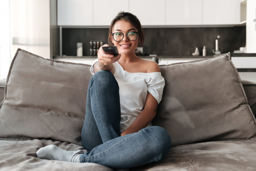 Qual é a melhor tv por assinatura do Brasil hoje 4 happy young woman sitting sofa home watch tv