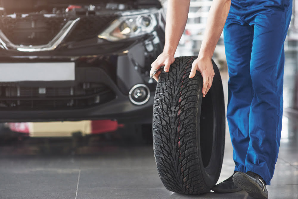 Como saber se meu carro precisa de manutenção? 4 technician with blue workwear holding wrench tire while showing thumb up