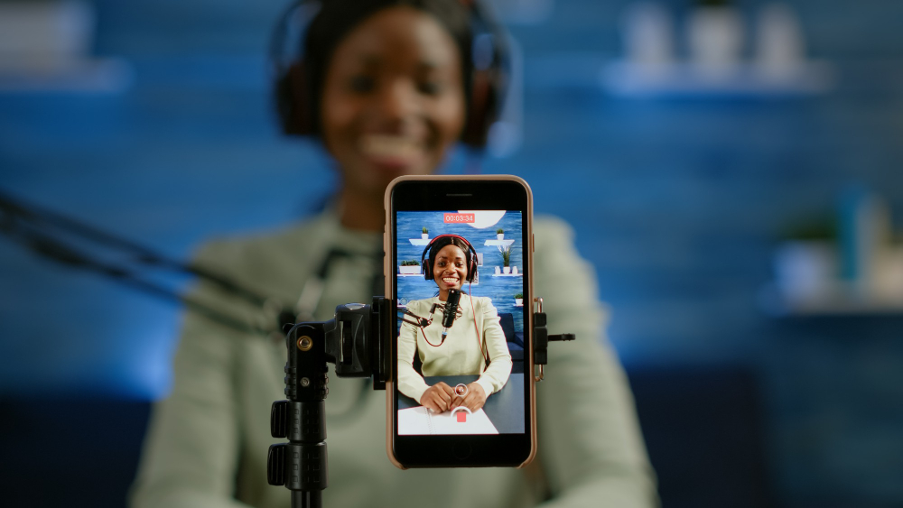 close up smartphone recording vlog african influencer home studio using smartphone speaking during livestreaming blogger discussing podcast wearing headphones professional microphone