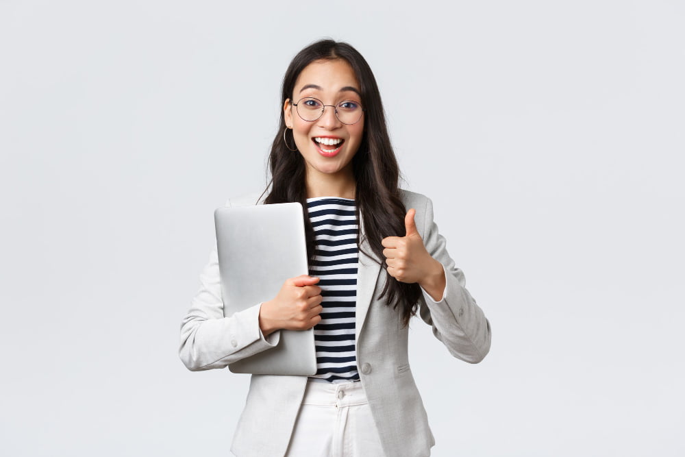 Como escolher o melhor software para gestão de qualidade? 1 business finance employment female successful entrepreneurs concept young confident businesswoman glasses showing thumbs up gesture hold laptop guarantee best service quality
