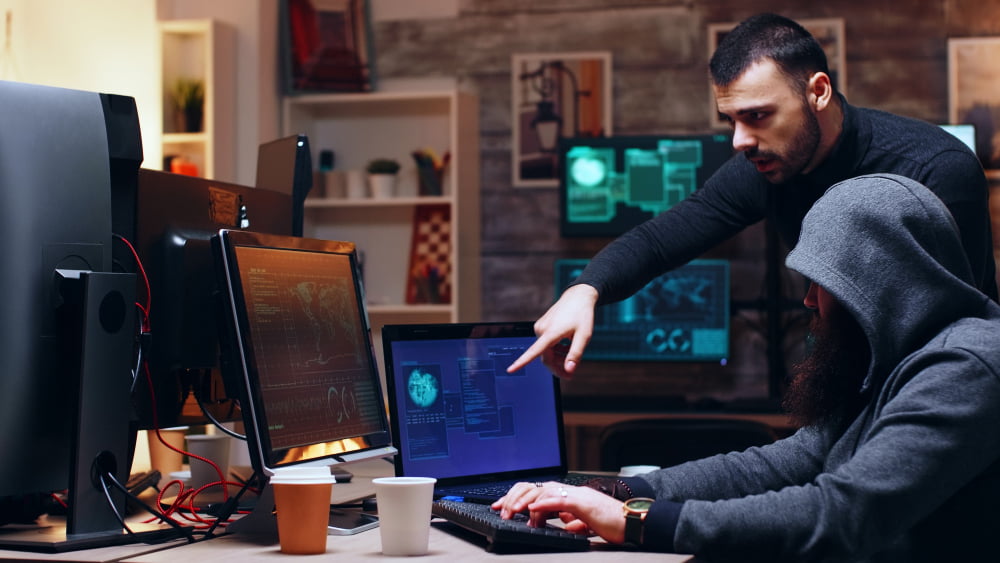 O que faz um Analista de Cibersegurança N1? 3 dangerous hooded hacker her partner hacking government planting malware