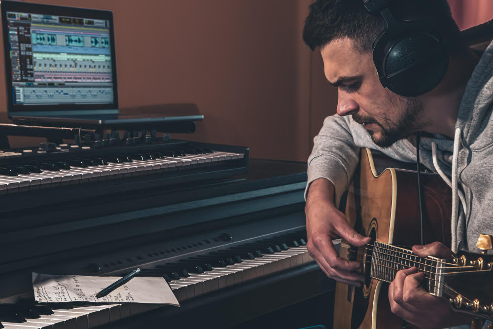 Como compor uma música romântica? 1 male musician plays guitar home workplace near computer 1