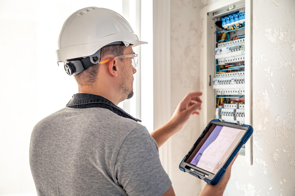 man electrical technician working switchboard with fuses uses tablet 2