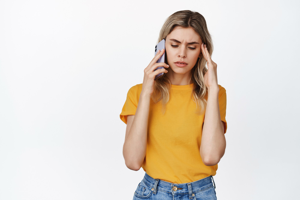 troubled young woman receive bad phone call holding smartphone near ear frowning upset standing white